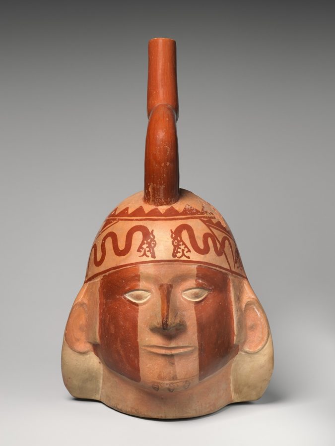 A human head in clay, painted red and cream, wearing a headdress patterned with snakes, with a spout rising from the top.