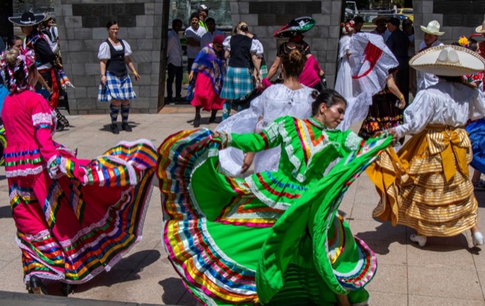 Dancers in full, brightly striped skirts spinning outdoors while a crowd watches.
