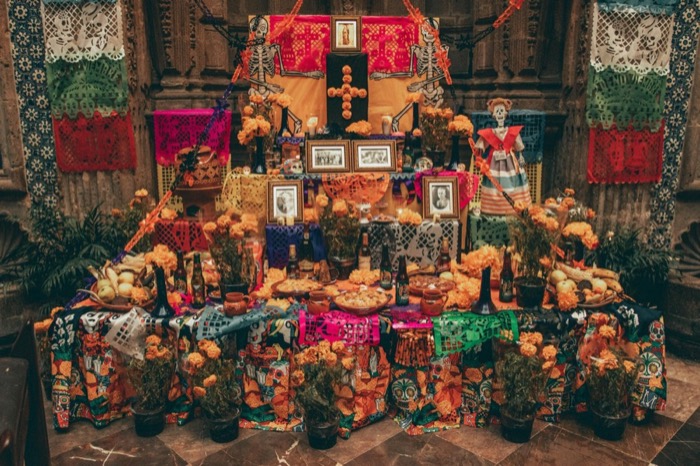 A Day of the Dead altar covered in marigolds, candles, framed photographs, food, and bright cut-paper banners.